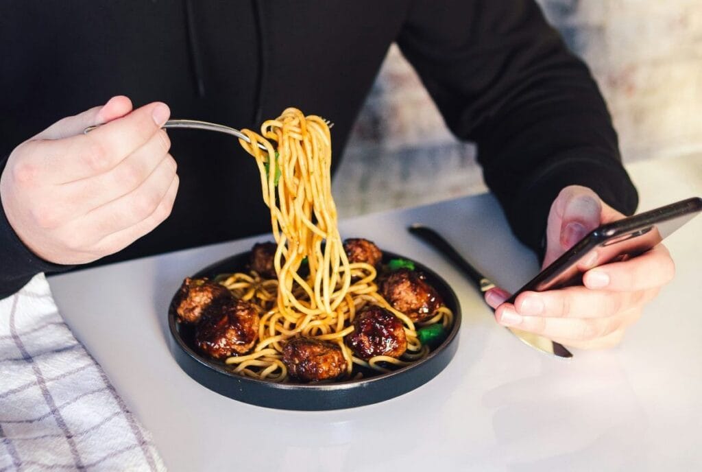 man eet bord met ramen terwijl hij zijn smartphone vasthoudt ter illustratie afvallen zonder dieet.