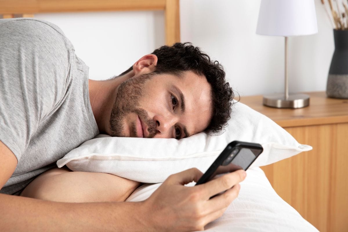Man scrolt op zijn telefoon voor tips tegen slapeloosheid in bed