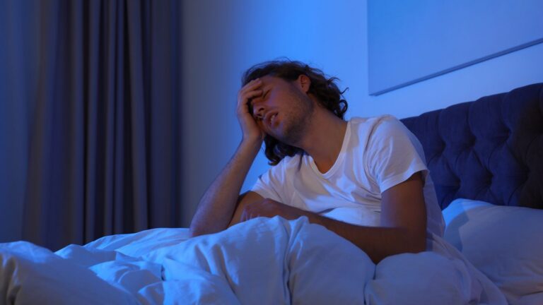 man zit wakker in bed omdat hij moeite heeft met doorslapen
